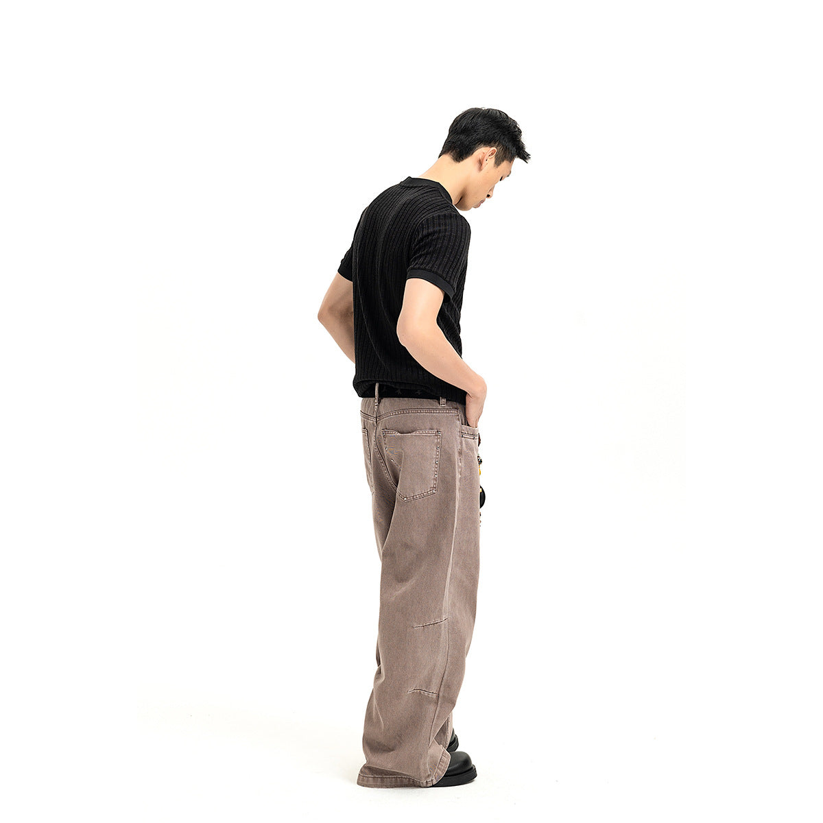 Side and rear view of a model wearing a black ribbed short-sleeve shirt and loose taupe jeans.