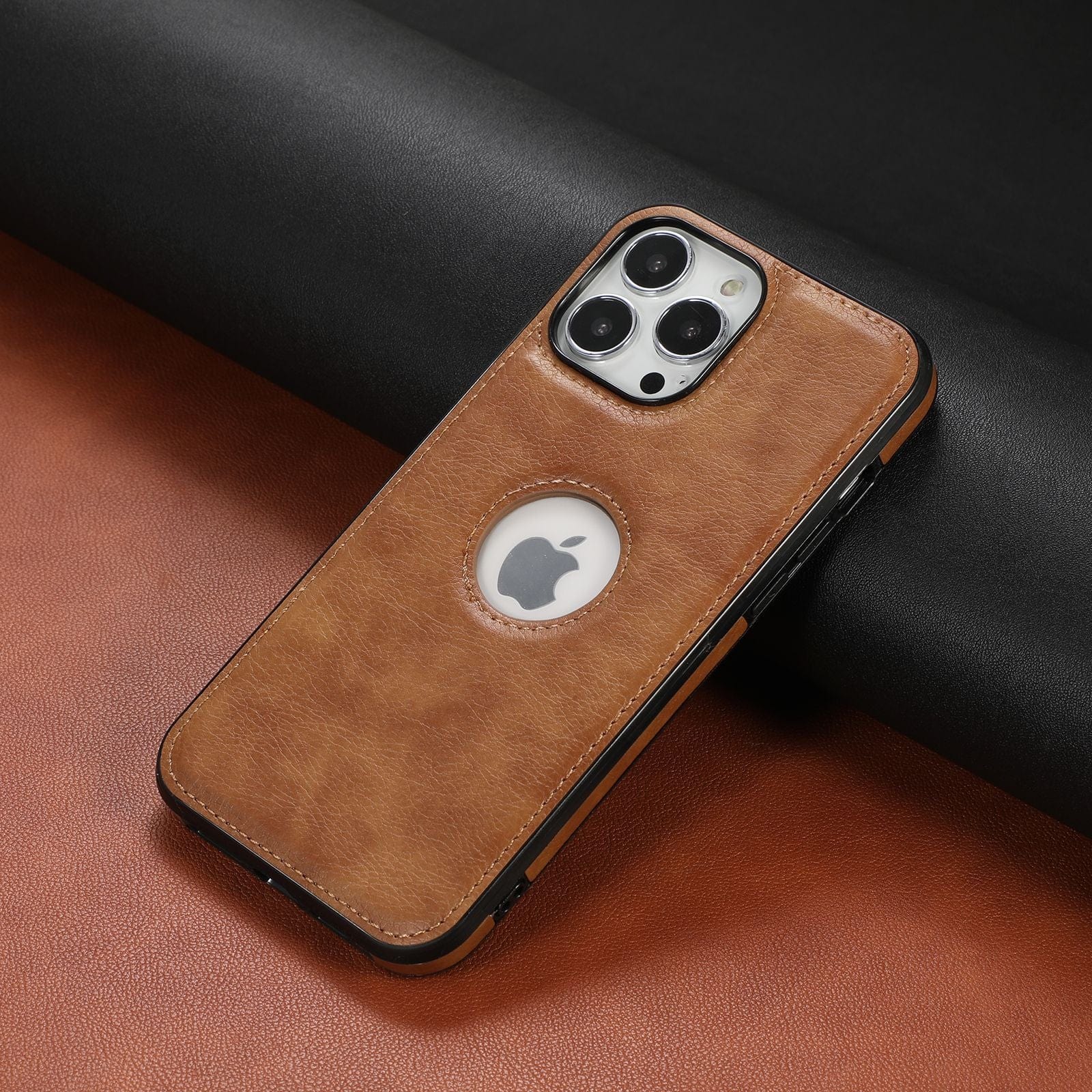 A smartphone encased in a Premium Synthetic Leather iPhone 16 Pro Max case, which is shockproof and anti-fingerprint, featuring a cutout that reveals the Apple logo on the back. The device rests on a surface with contrasting black and brown sections.
