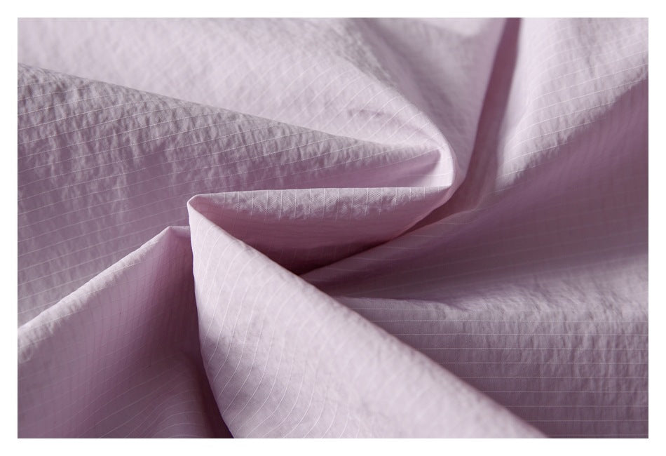 Close-up of pale pink fabric showing fine grid lines, folds, and stitching.