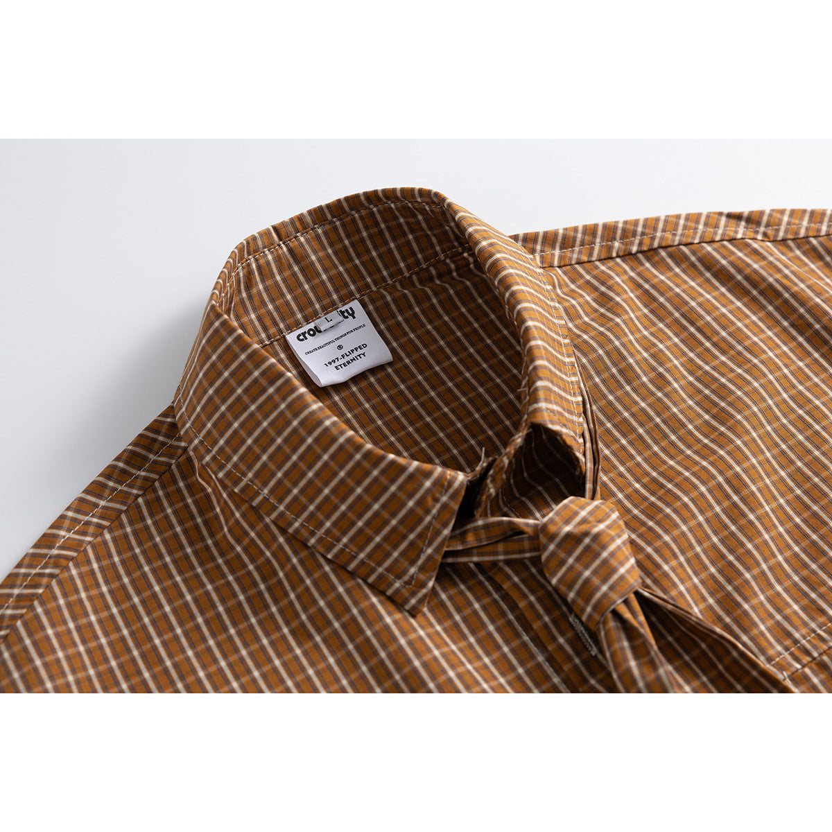 Close-up of a brown and orange plaid shirt collar and sewn-in neck label.