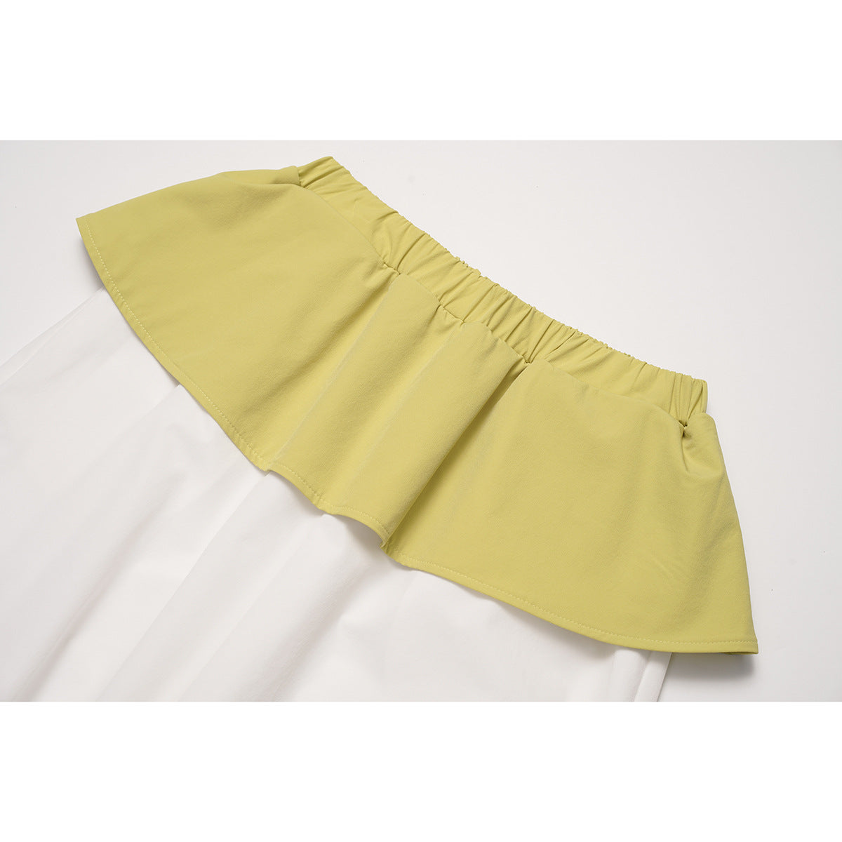 Close-up of the gathered yellow flounced waistband over white pants.