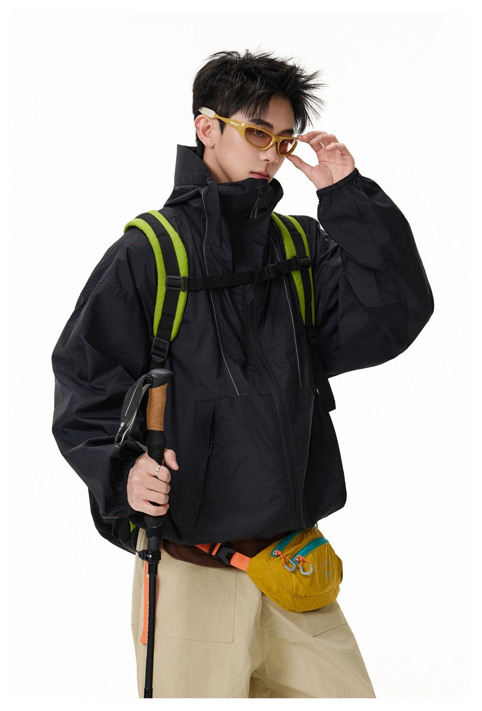 Model wearing an oversized black zip-front jacket with a high collar and lime-green backpack straps.