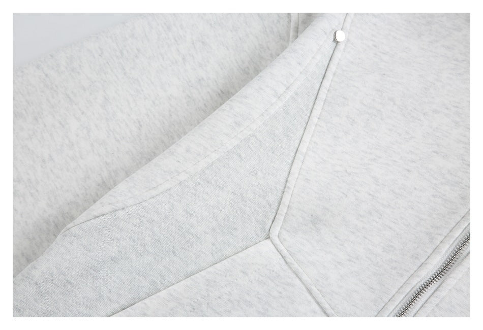 Close-up of light gray heather garment panels, a metal snap, stitched seams, and part of a zipper.