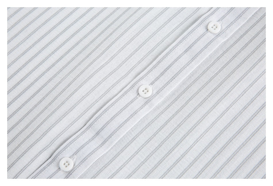 Close-up of a white garment with fine gray stripes and three white buttons along a placket.