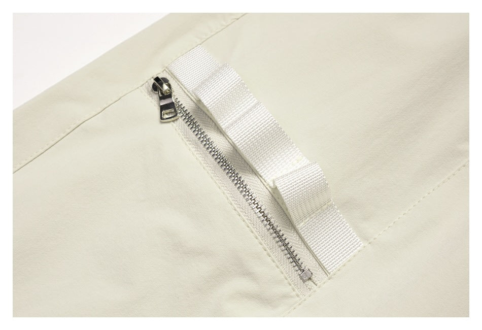 Close-up of a metal zipper and woven pull tab on the off-white pants.