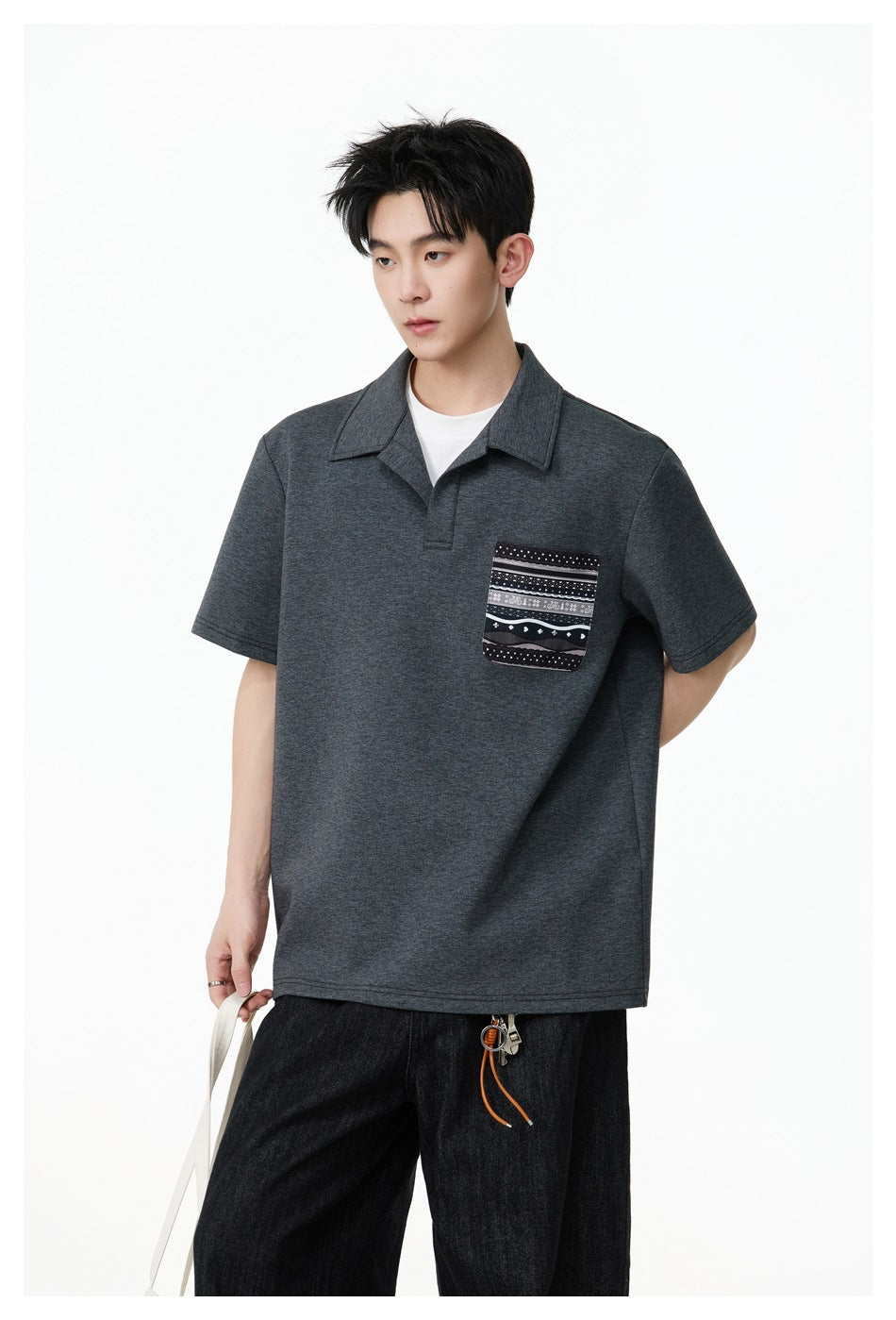 Closer view of a model wearing a charcoal polo with a pointed collar and a black-and-white patterned chest pocket.