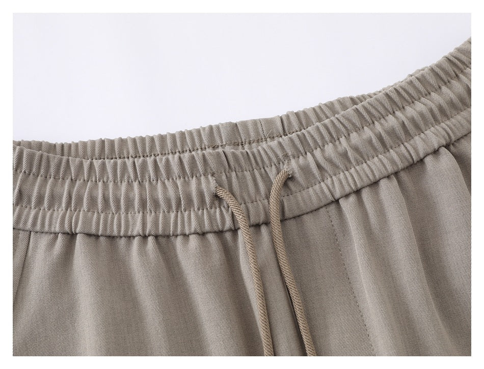 Close-up of taupe shorts showing the gathered elastic waistband, stitching, and drawstrings.