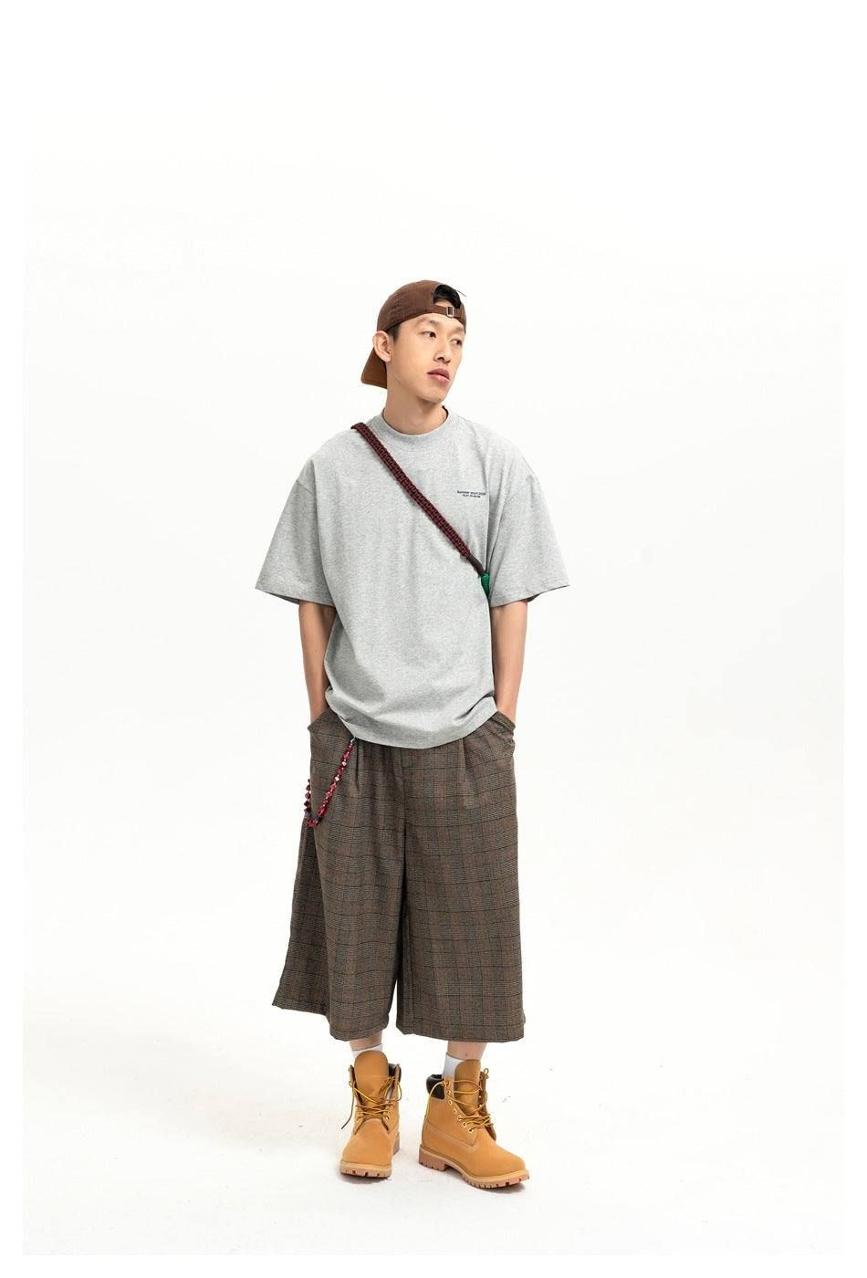 Full-length front view of a model in a light gray oversized T-shirt and brown plaid shorts.