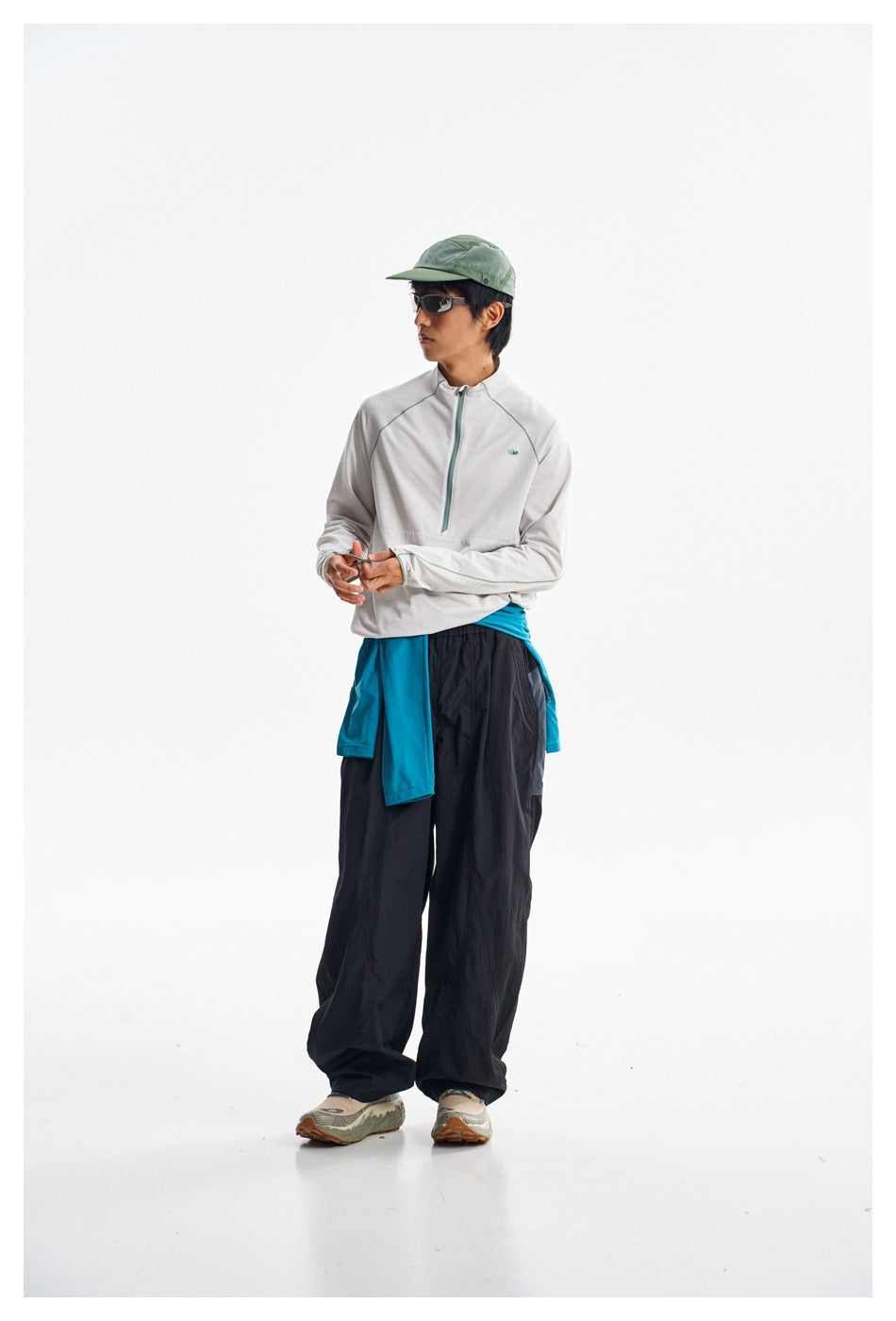 Model in a white zip-neck pullover and loose black pants, with a turquoise layer tied at the waist.