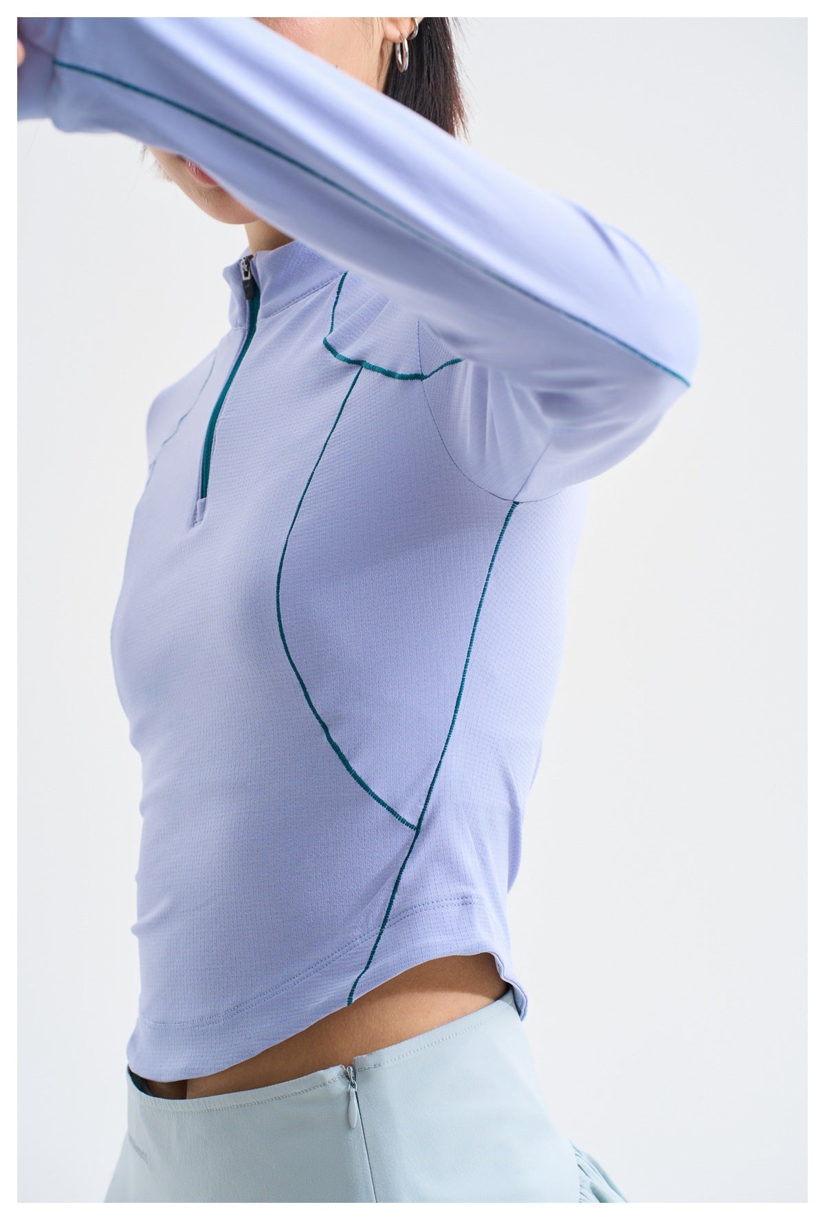 Close-up of a lilac quarter-zip top, showing its teal piping, textured fabric, and sleeve detail.
