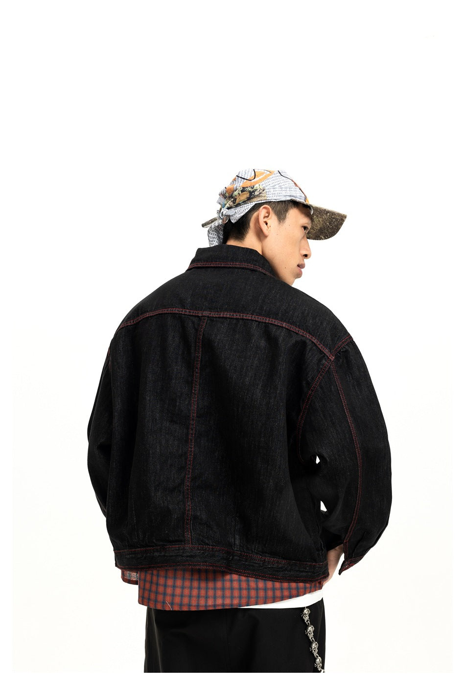 Rear view of a model wearing a black jacket with red seam stitching and a plaid shirt visible below the hem.