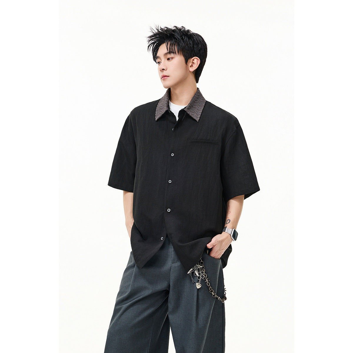 Model wearing a black short-sleeve button-up shirt with a textured gray collar and chest pocket, paired with dark wide-leg