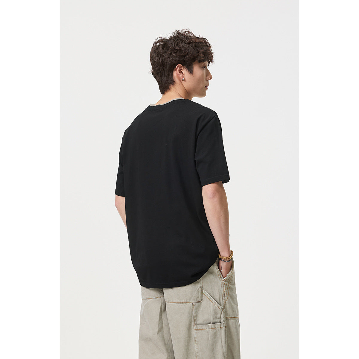 Rear view of a model wearing a plain black short-sleeve T-shirt with a layered gray neckline.
