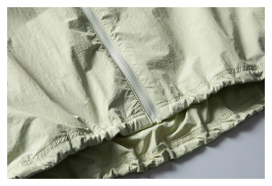 Close-up of a pale sage jacket's front zipper and gathered lower hem.