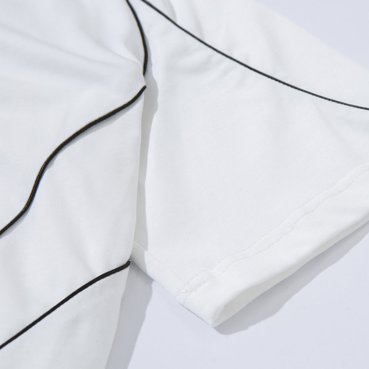 Close-up of a white T-shirt’s sleeve and hem with narrow black piping.