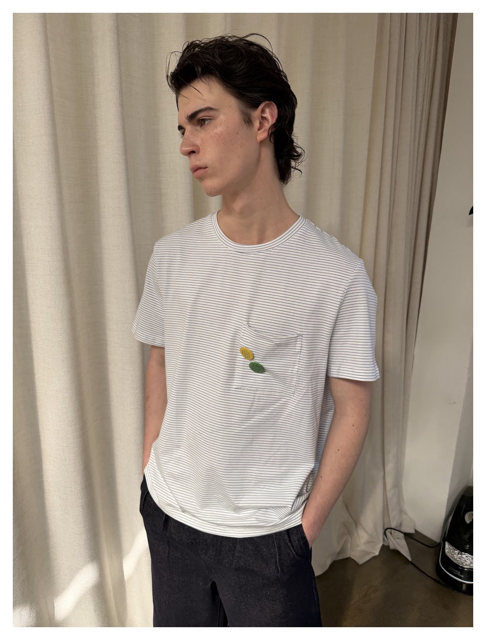 Close view of a white T-shirt with fine gray stripes, chest pocket and small yellow and green accents.