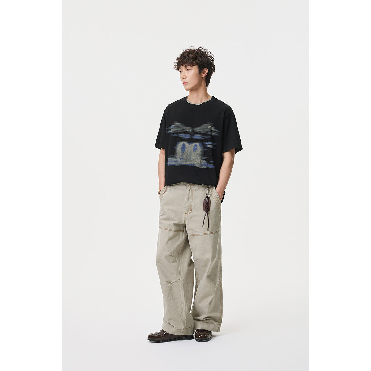 Full-length model wearing a black graphic T-shirt, loose beige cargo trousers, and dark shoes.