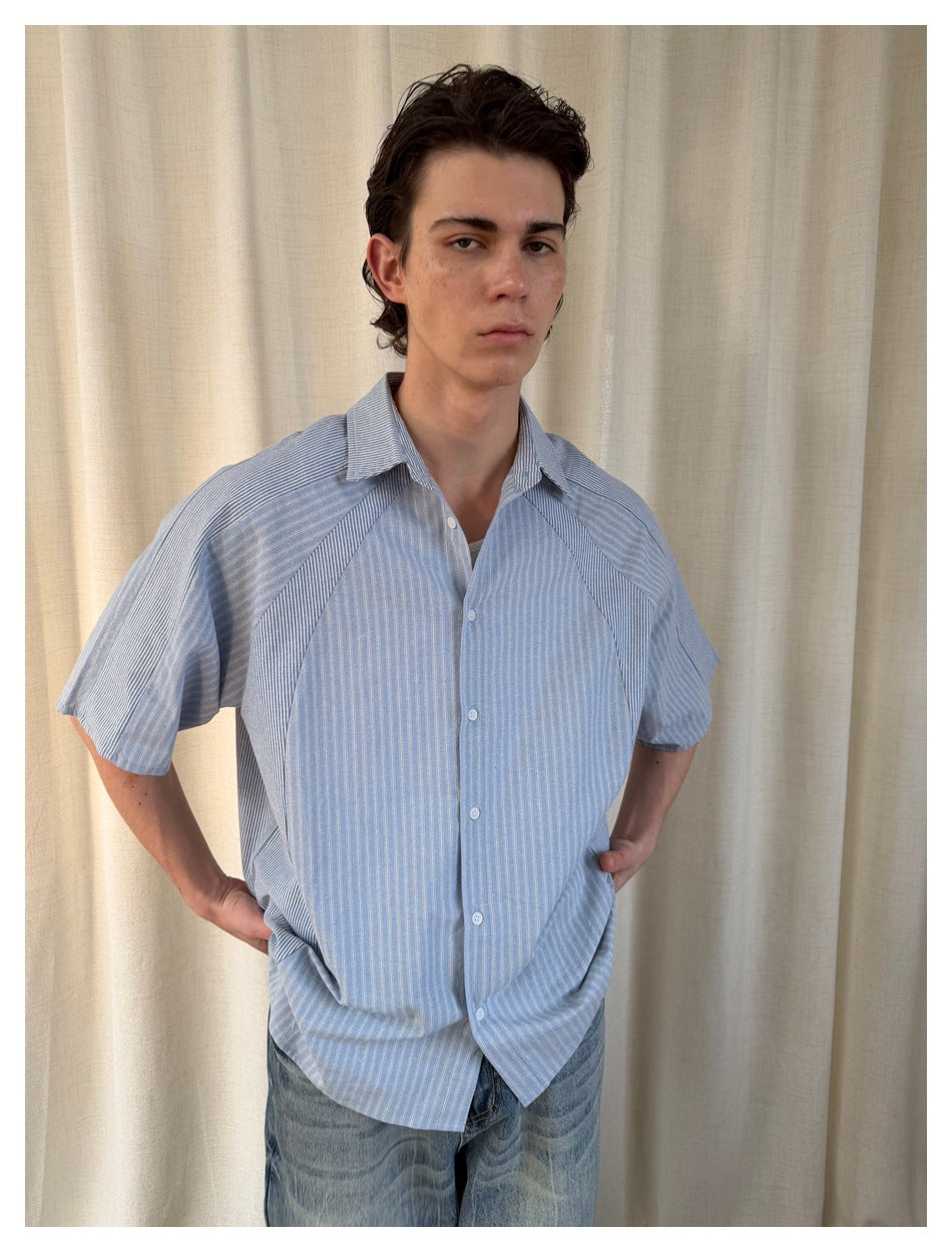 Close front view of a person wearing a light blue striped shirt with a collar, buttons, and contrasting raglan panels.