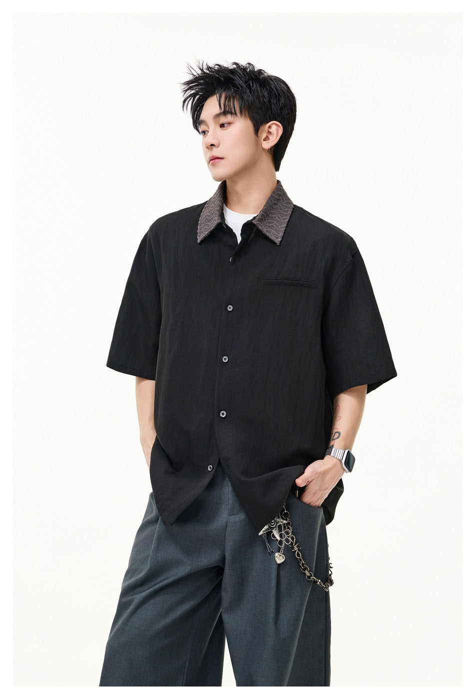 Model wearing black short-sleeve shirt with gray textured collar, gray trousers and a chain accessory