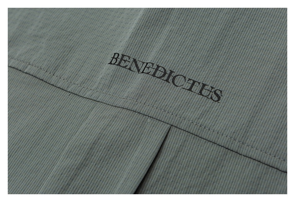 Close-up of a black BENEDICTUS logo above a stitched seam on muted gray-green ribbed fabric.