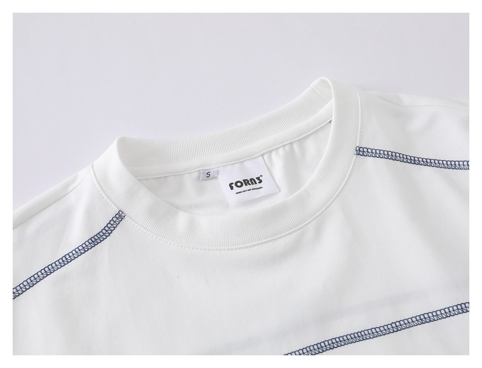 Close-up of a white crew-neck T-shirt with dark contrast seams and a visible neck label.