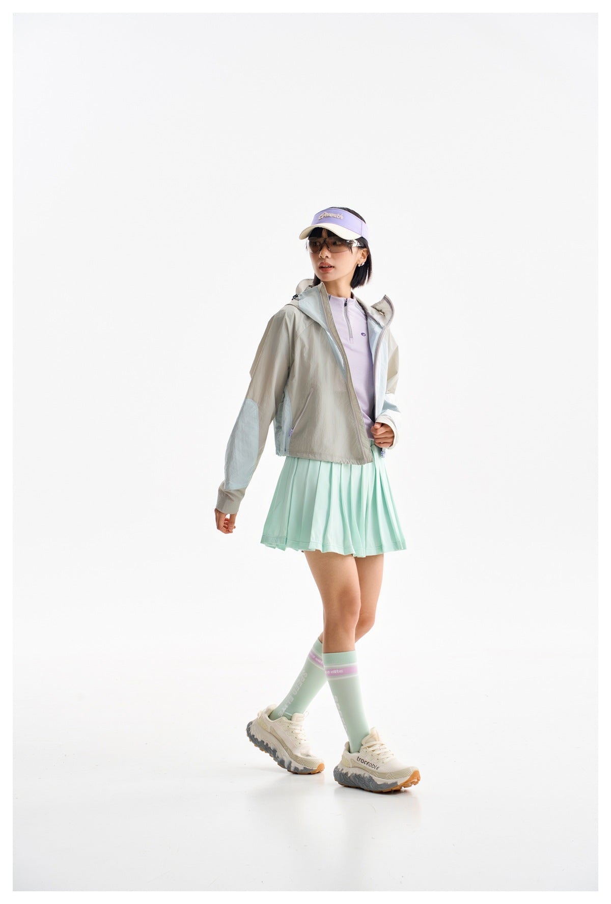 Model walking in a gray and pale blue hooded jacket with a mint pleated skirt.