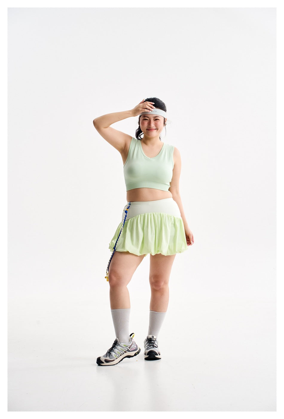 Full-length front view of a model wearing a pale mint crop top and light green bubble-hem tennis skirt.