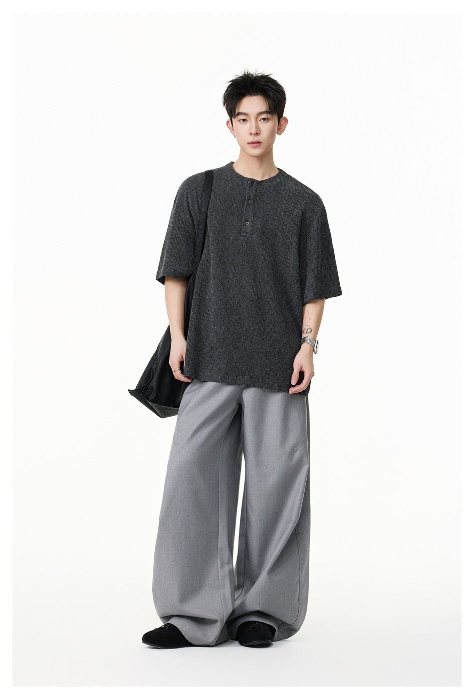 Full-length model wearing a charcoal oversized short-sleeve top with a two-button placket and gray wide-leg trousers.