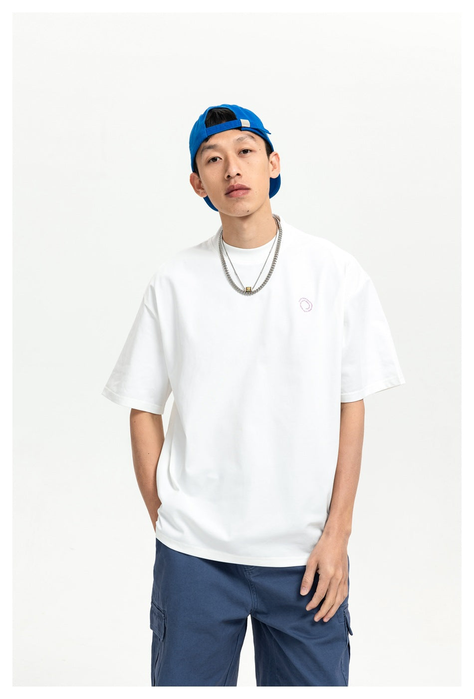 Waist-up front view of a man wearing a white oversized T-shirt with a small chest emblem.