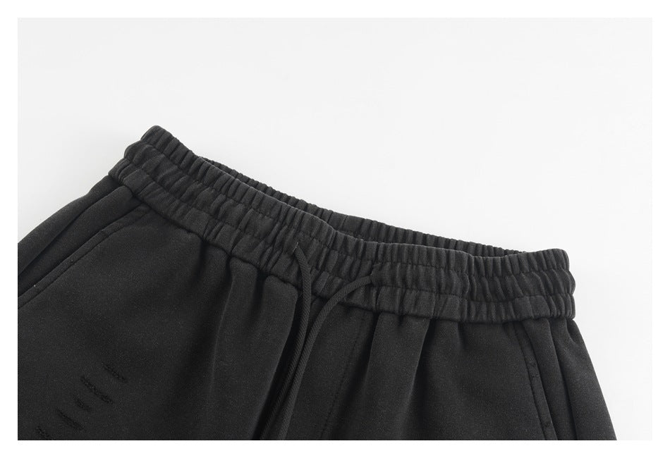 Close-up of black shorts showing the elastic waistband, drawstring, side pocket, and subtle distressed marks.