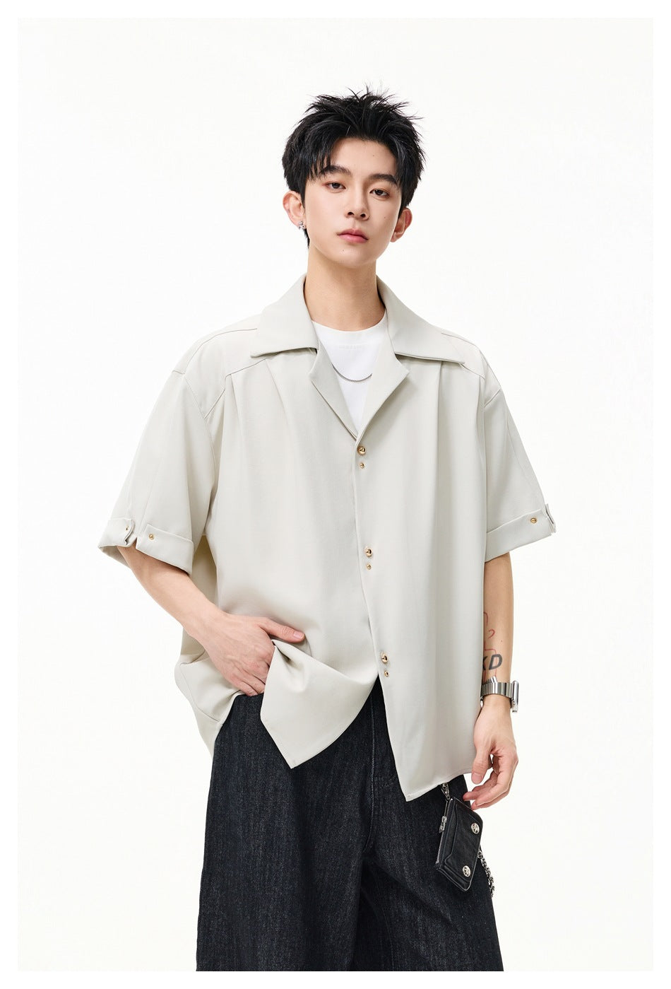 Model wearing a light cream oversized short-sleeve shirt with wide lapels, gold-tone buttons, and rolled cuffs.