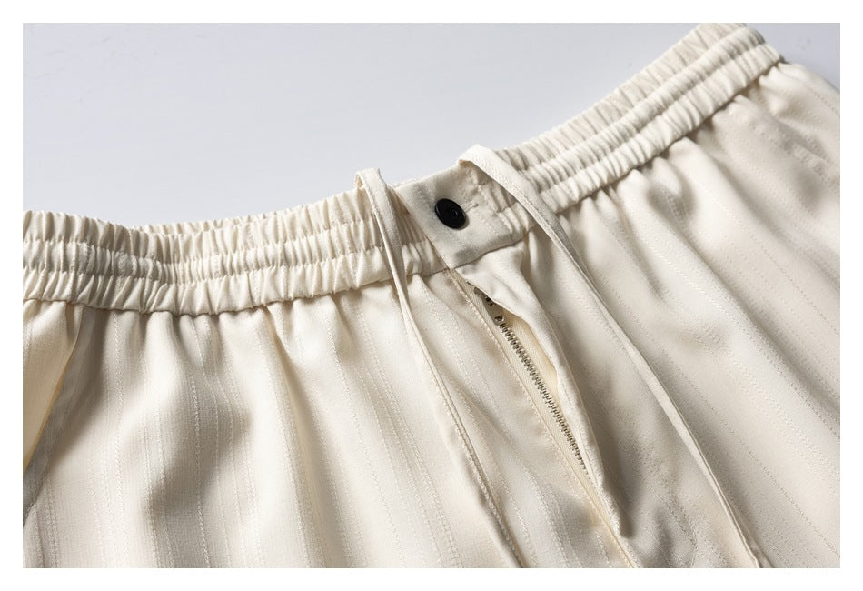 Close-up of cream striped shorts showing an elastic waistband, drawstring, black button and zip fly.