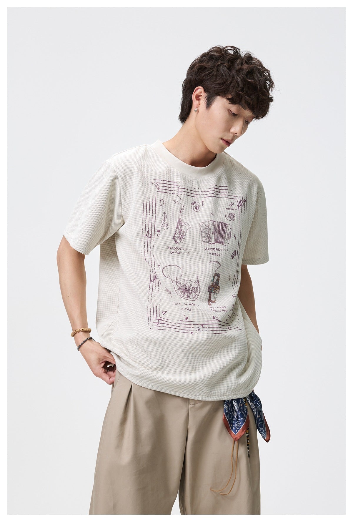 Man looking down wearing beige waffle-knit graphic T-shirt with khaki pleated trousers and a paisley scarf