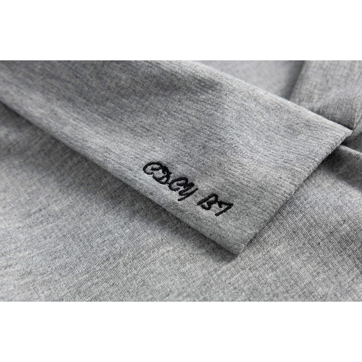 Close-up of black embroidered lettering on the crossover collar of a heather-gray top.