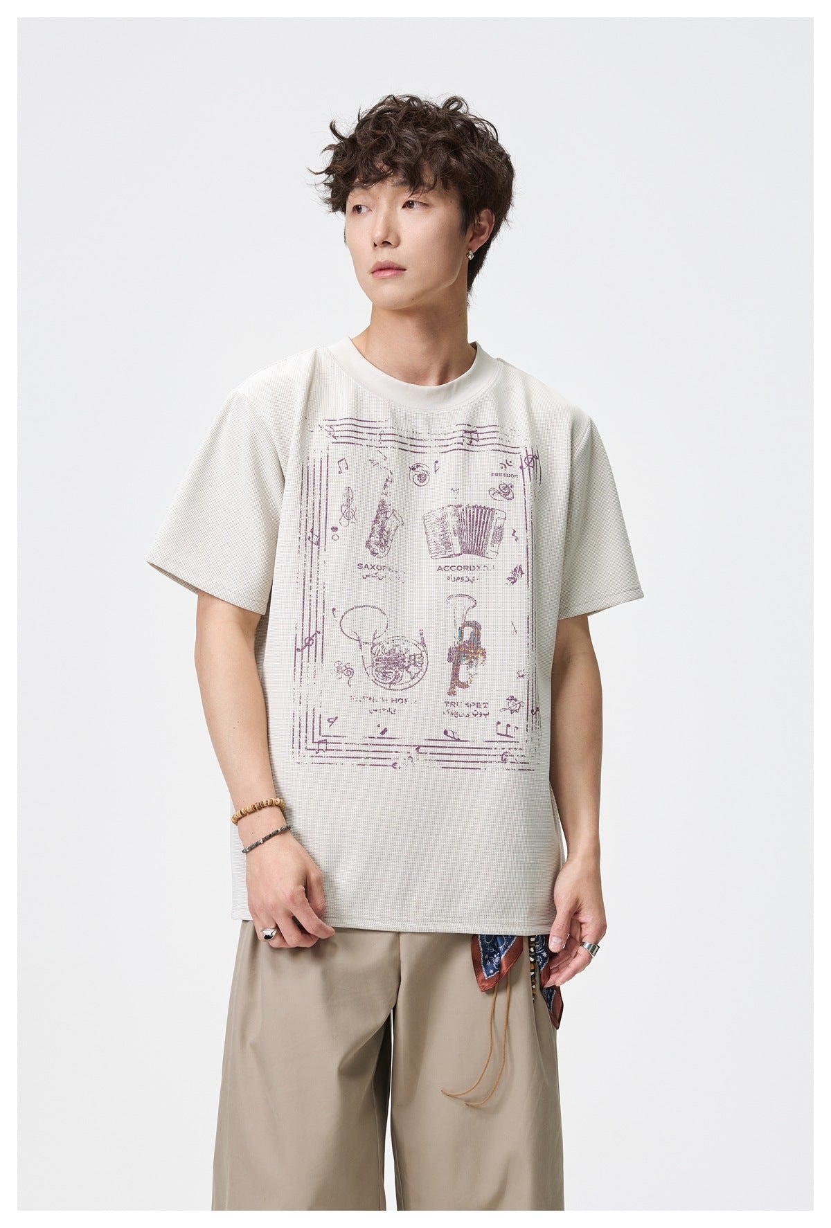 Man wearing beige waffle-knit T-shirt with musical instrument graphic and khaki wide trousers, front view