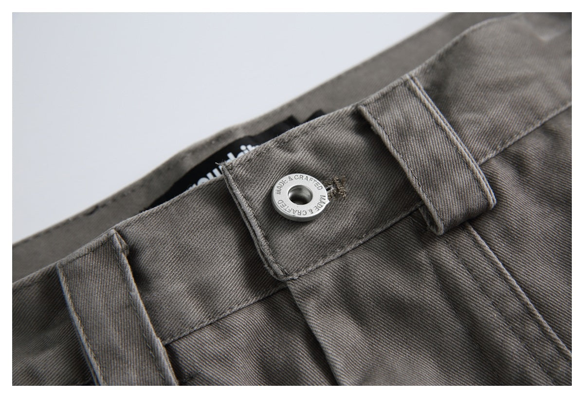 Close-up of charcoal-gray trousers showing the waistband, belt loops, and a silver button with engraved lettering.