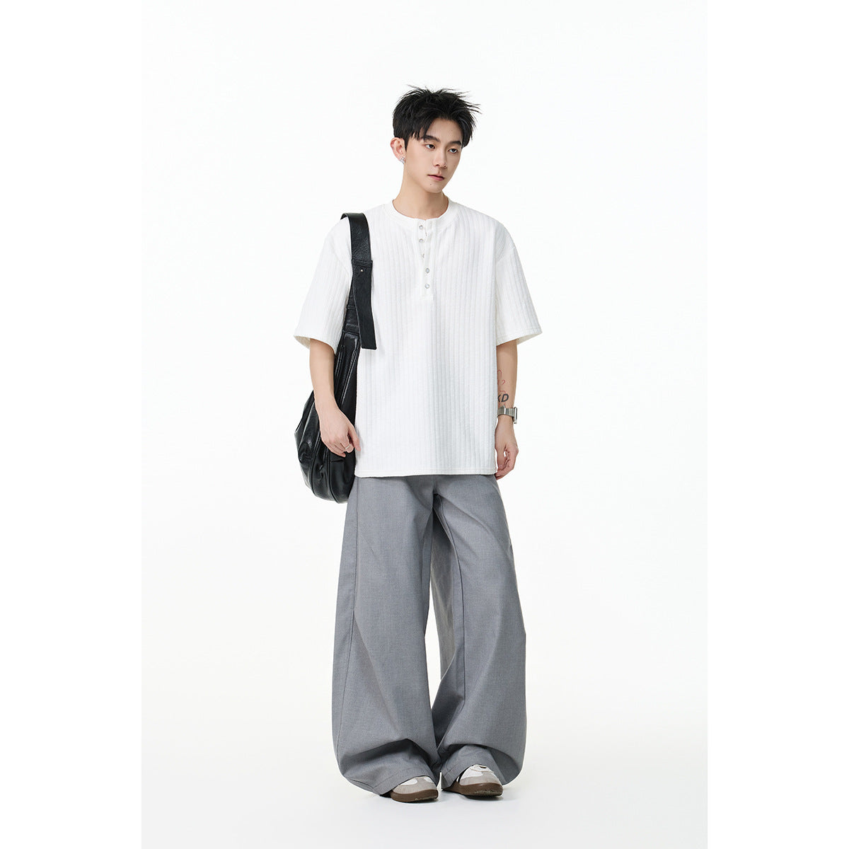 Model wearing a loose white ribbed short-sleeve henley and gray wide-leg trousers with a black shoulder bag.