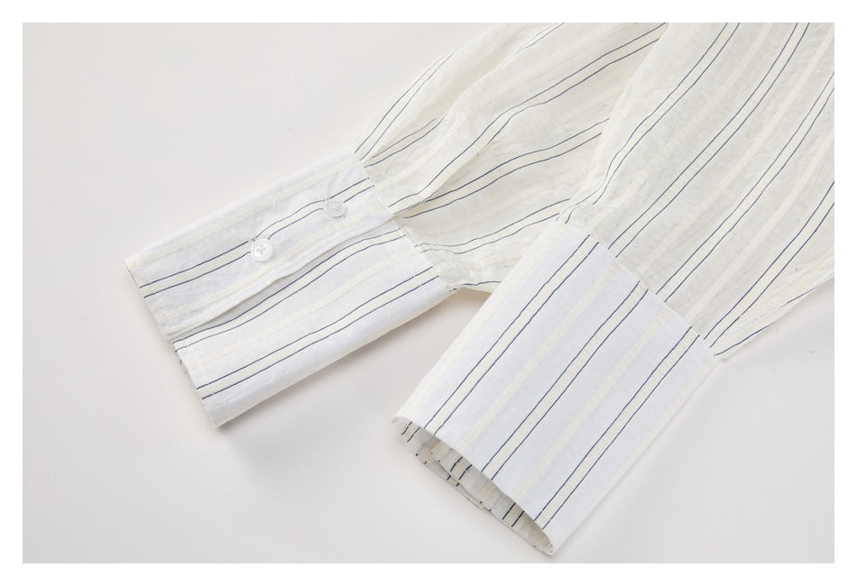 Close-up of the long sleeves and buttoned cuffs of an ivory shirt with thin navy stripes.