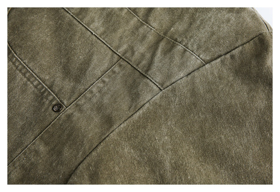 Close-up of olive-gray garment fabric with intersecting seams and a small dark button.