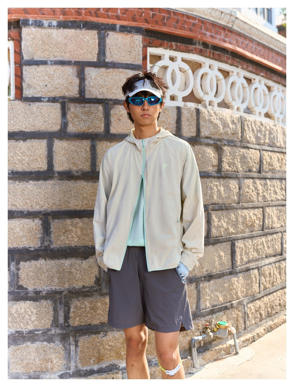Model wearing a light beige hooded jacket with pale aqua trim and dark shorts outdoors.