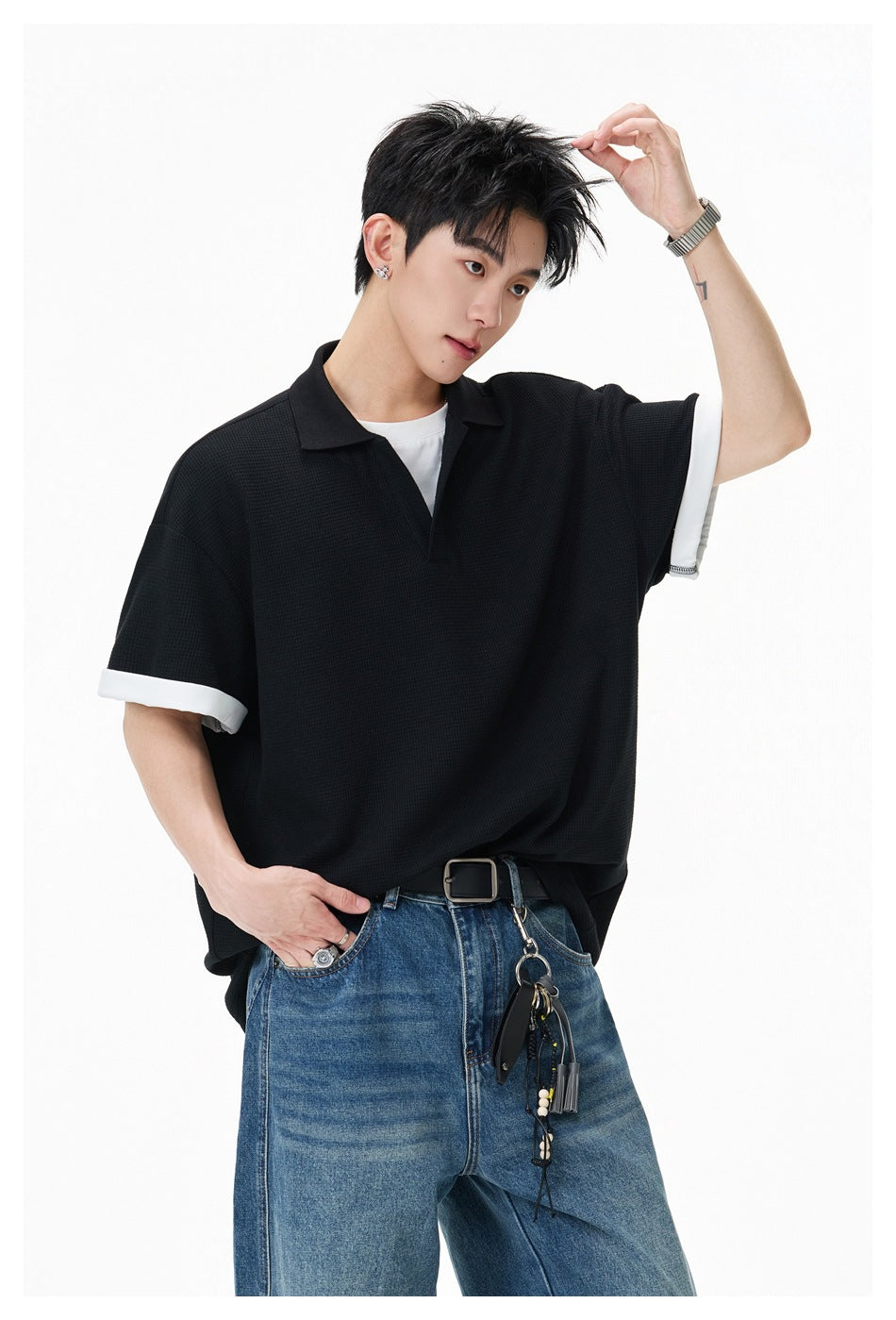 Angled close view of a model wearing a black polo with a collar and white sleeve cuffs.