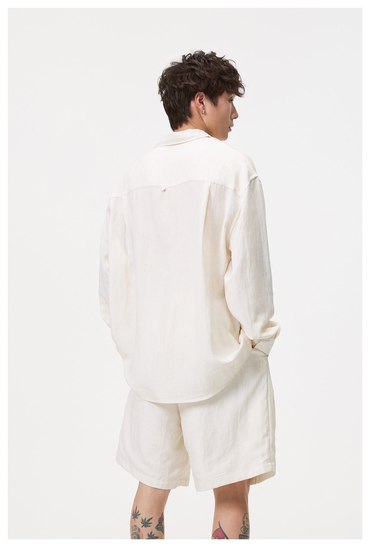 Closer back view of a man wearing an off-white long-sleeve shirt and matching shorts.