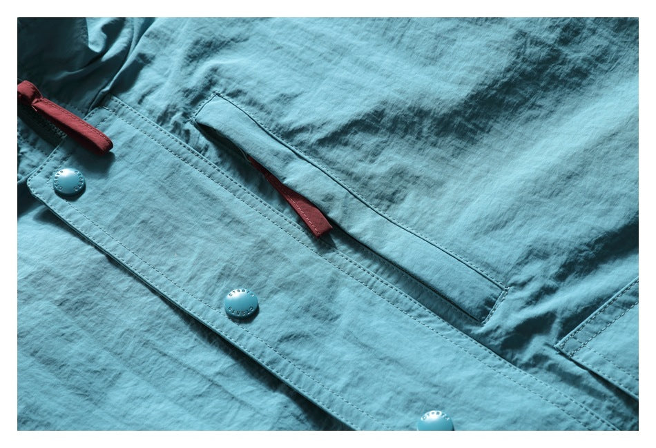 Close-up of a teal jacket front with snap buttons, a pocket opening, and red zipper pulls.