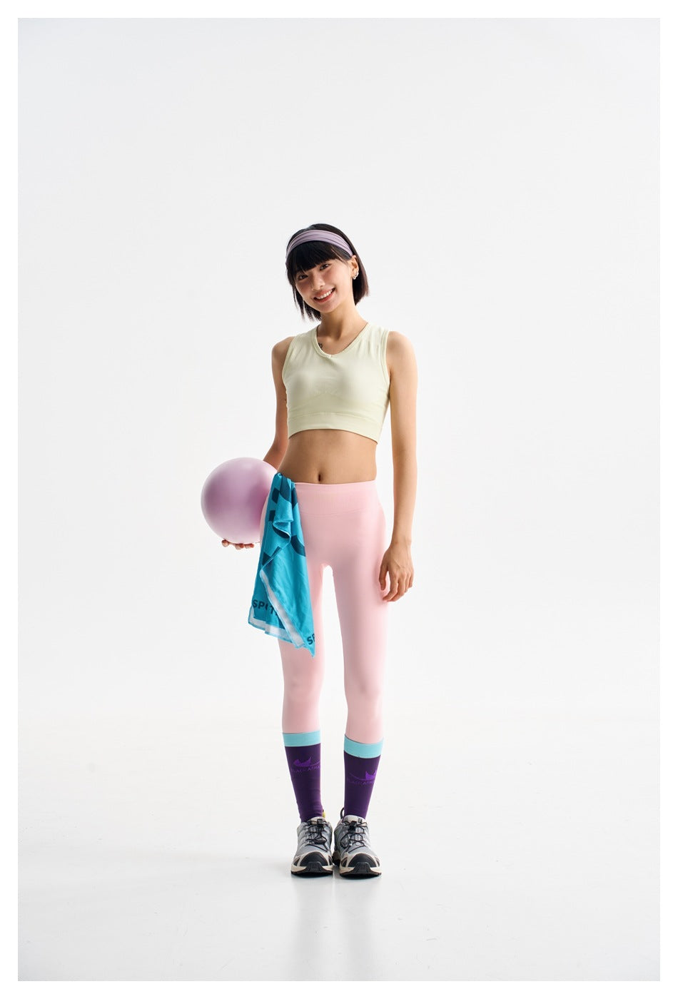 Model wearing a pale yellow-green sleeveless crop top and pink leggings with purple-and-teal knee socks.