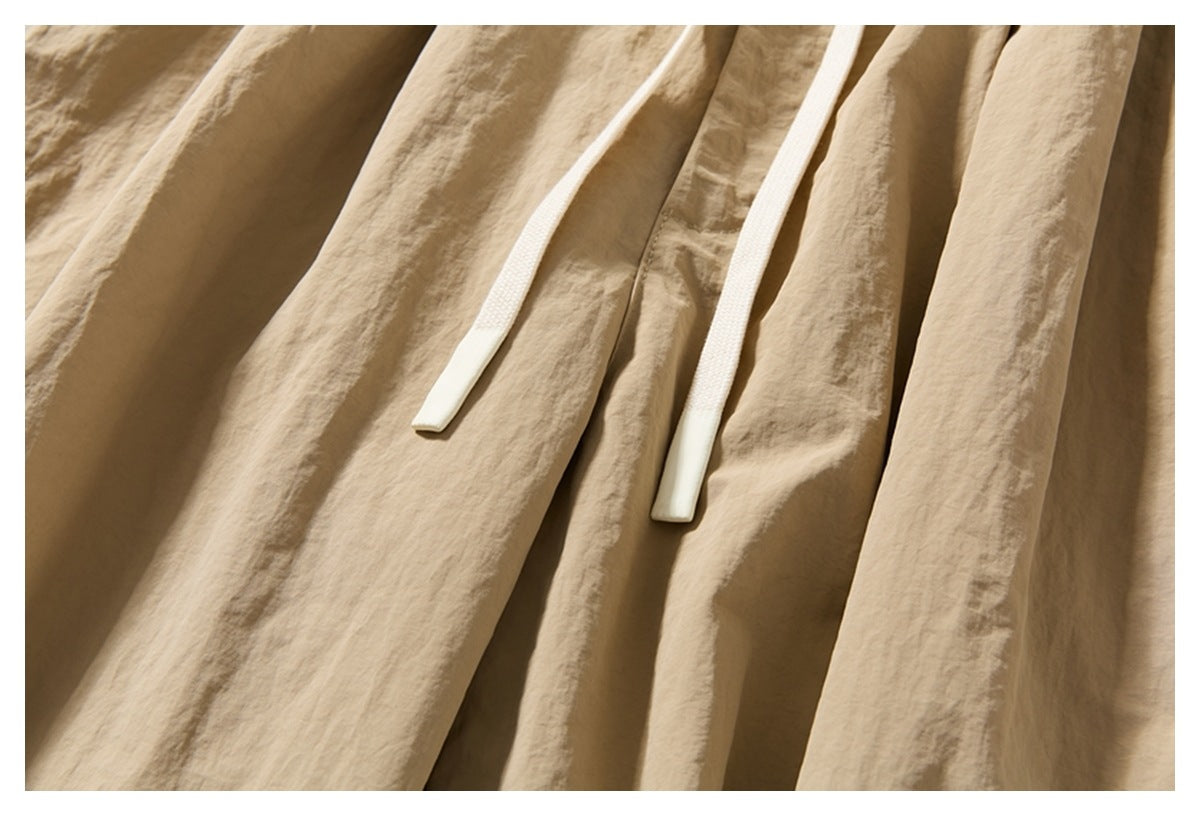 Close-up of beige trousers showing two long cream drawstrings against the gathered fabric.