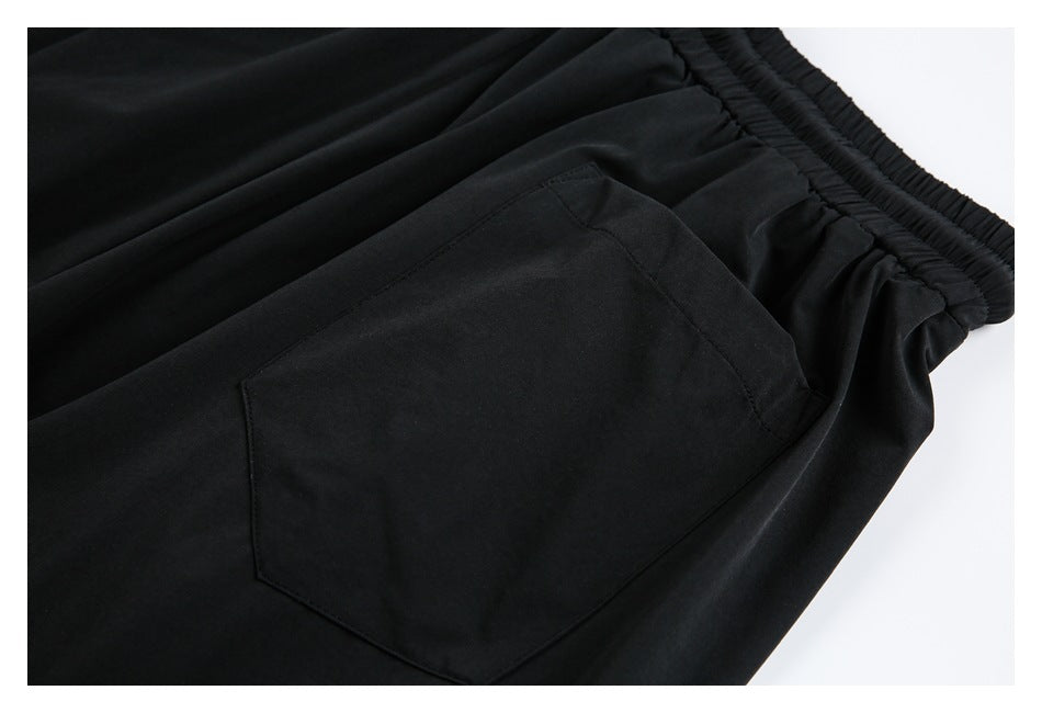 Close-up of black trousers showing an elastic waistband and a large stitched pocket.
