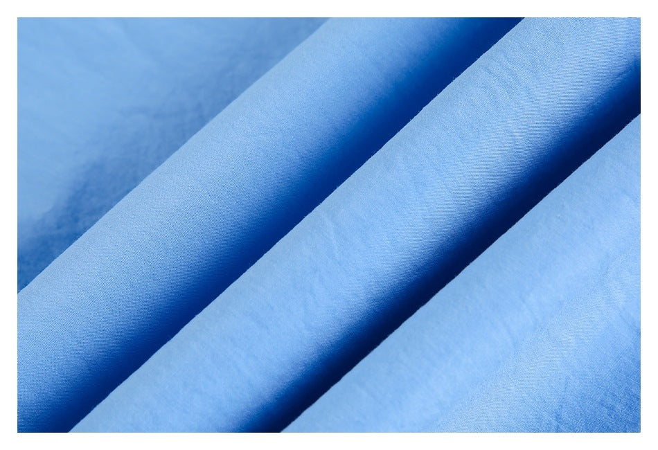 Close-up of light blue garment fabric draped in folds, showing its surface texture.