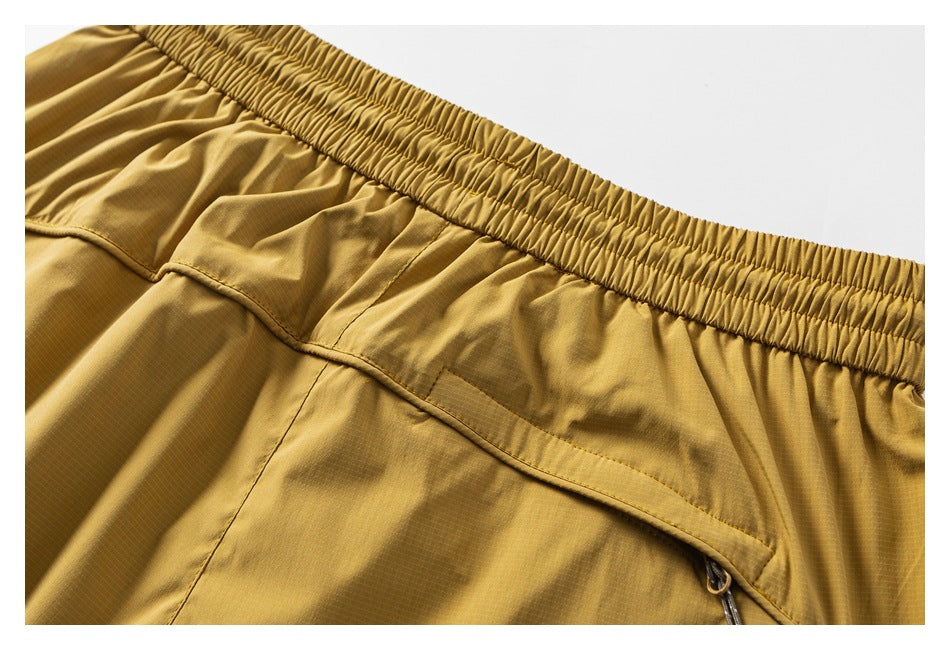 Close-up of mustard-gold trousers with an elastic waistband and a zippered pocket.