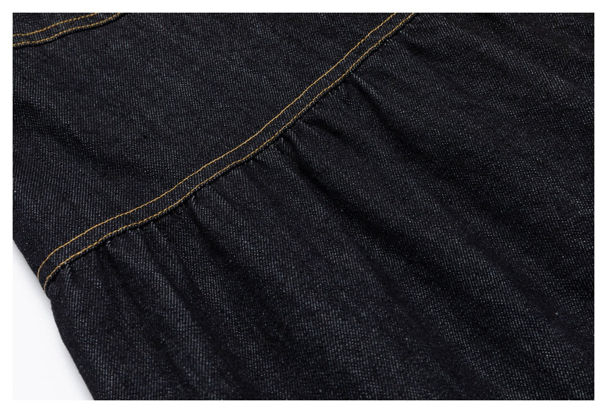 Close-up of dark denim fabric and a curved seam with golden stitching.