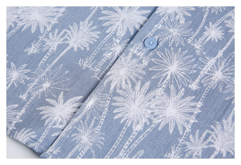 Close-up of the light blue garment's white palm-tree pattern, button, and stitched edge.